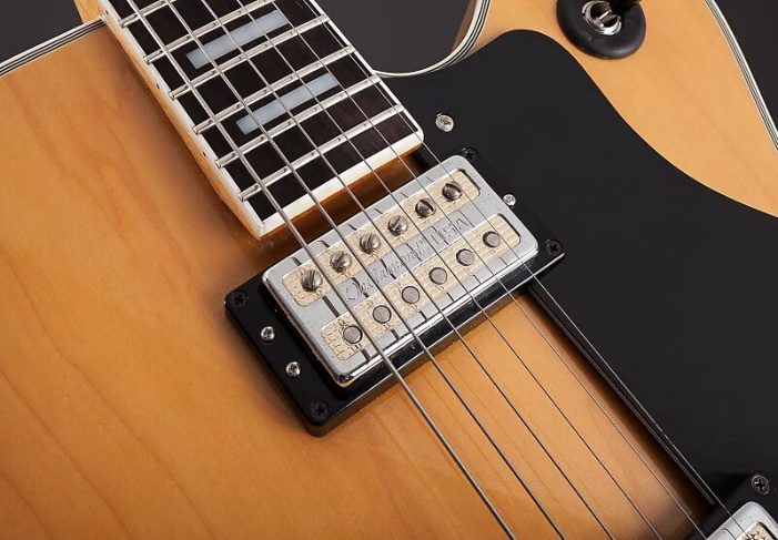 Close-up of an electric guitar featuring a wooden body, a black pickguard, and a metal bridge with adjustable saddles, highlighting its craftsmanship.